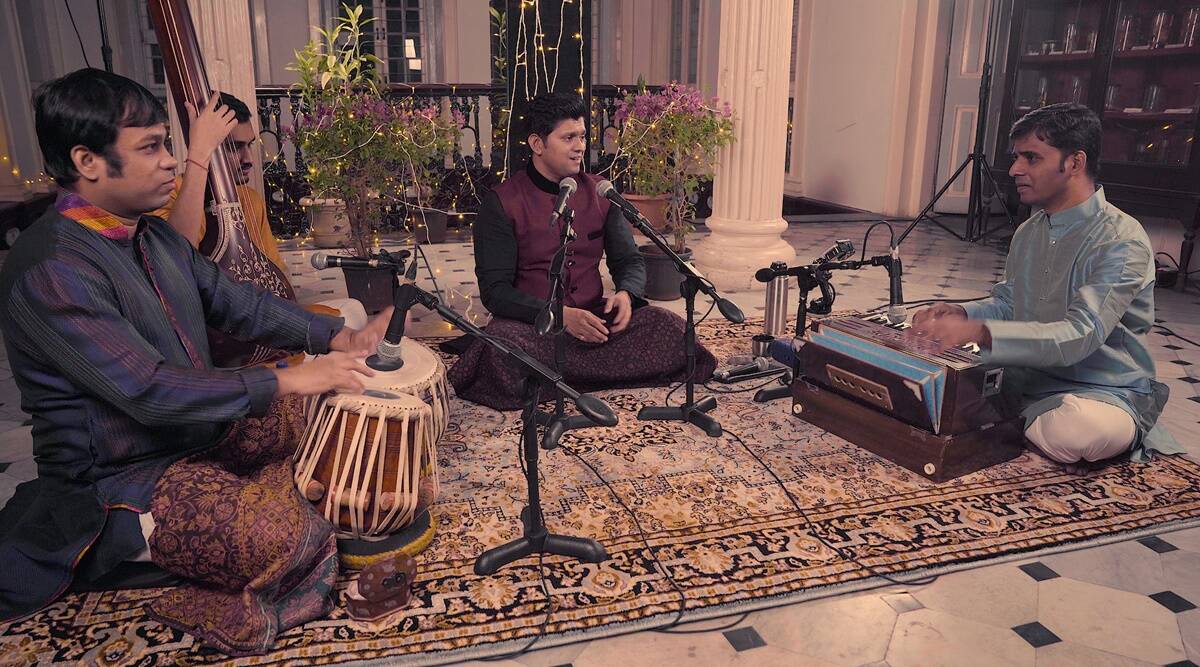 Four musicians sit on the floor in traditional Indian dress, performing music