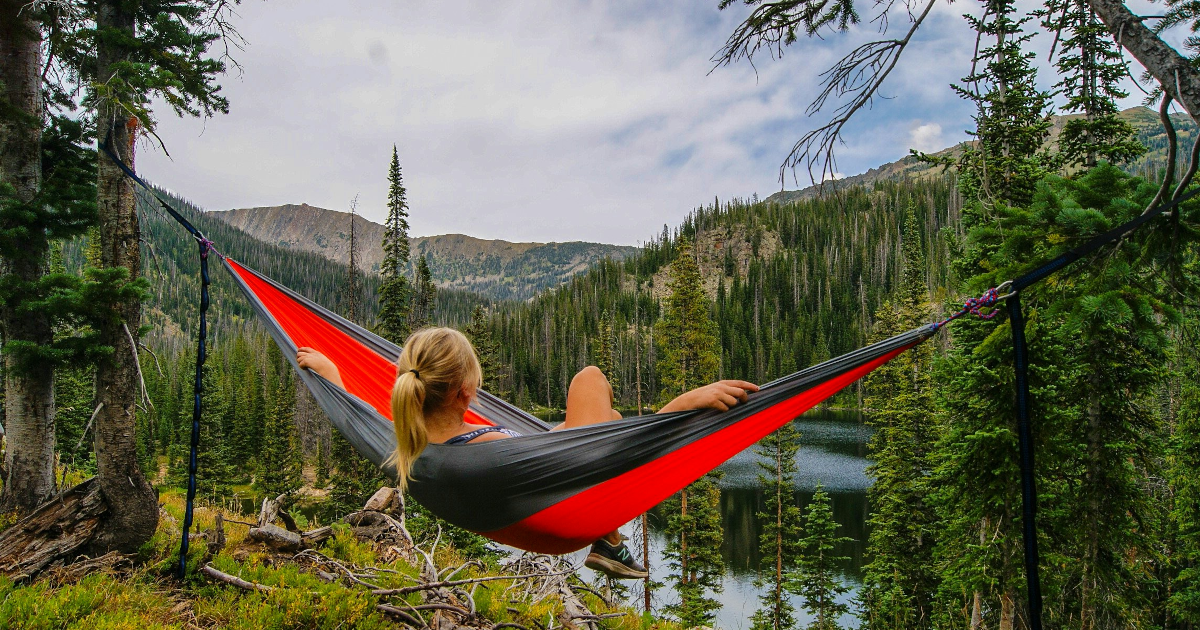 A person sits in a hammock overlooking a mountain lake